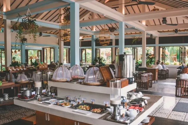 An open pavilion with pale blue pillars, a buffet counter under domed covers and a wooden beam ceiling