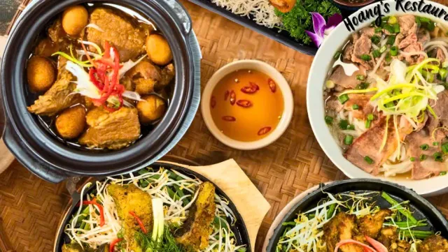 An overhead view of a clay pot with meat and eggs, a noodle soup bowl and more dishes