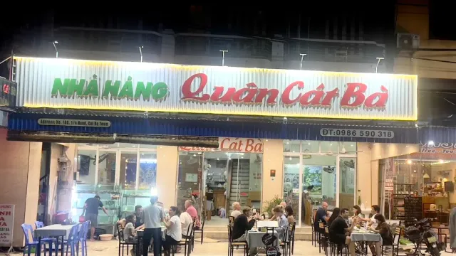 A lit front with a large sign at night, diners at tables on the sidewalk