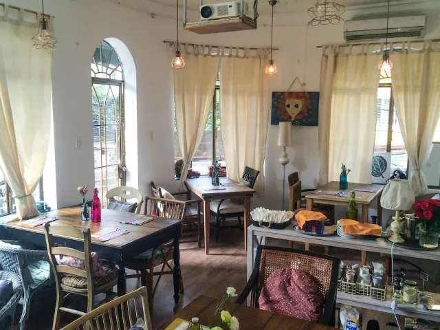 A bright room with cream curtains, an arched window, hanging bulbs and assorted wooden tables