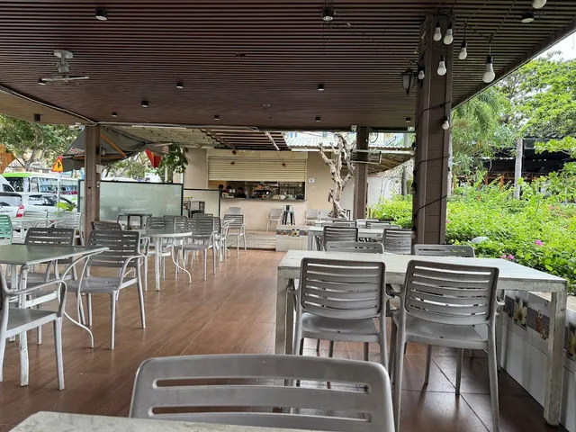 A covered terrace with white tables and chairs, and green plants along the side