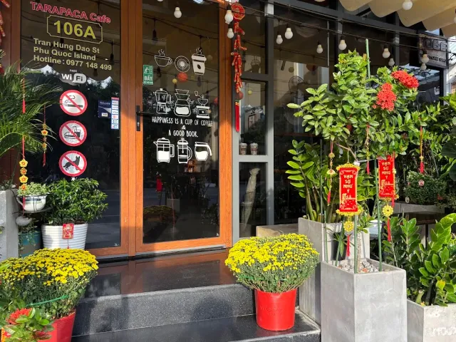 A glass storefront with a red sign, white drawings of brewing gear on the window and yellow chrysanthemums