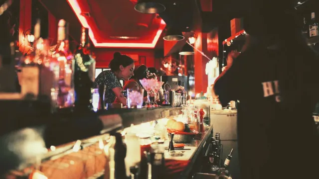 A dark bar counter under red neon strips, bartenders preparing drinks behind it