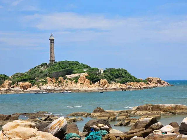 A lighthouse on a green island, granite boulders in the foreground and fishing nets among the rocks