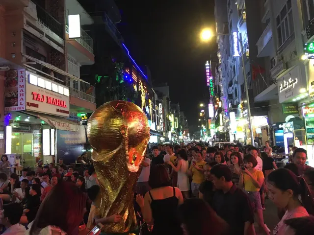 A night street crowded with people, neon signs and a gilded statue