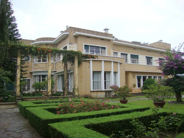 A cream two story villa with rounded lines, a geometric hedge garden and roses