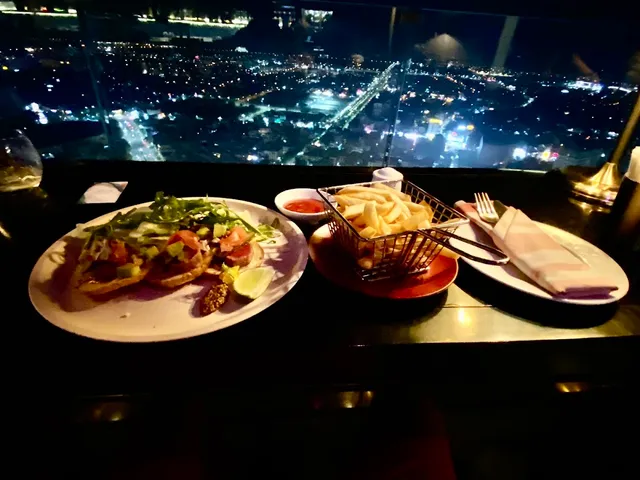 Plates of food and a basket of fries on a table facing the city lights at night
