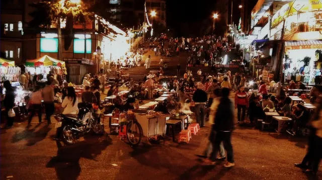 Lit night market stalls with shoppers and scooters