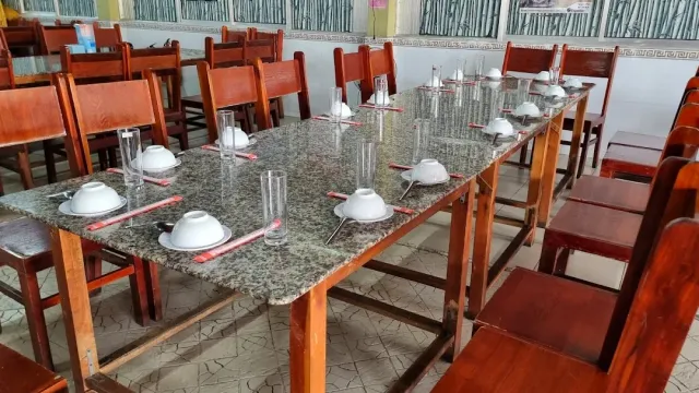 An empty hall with long stone topped tables, wooden chairs and white bowls laid out