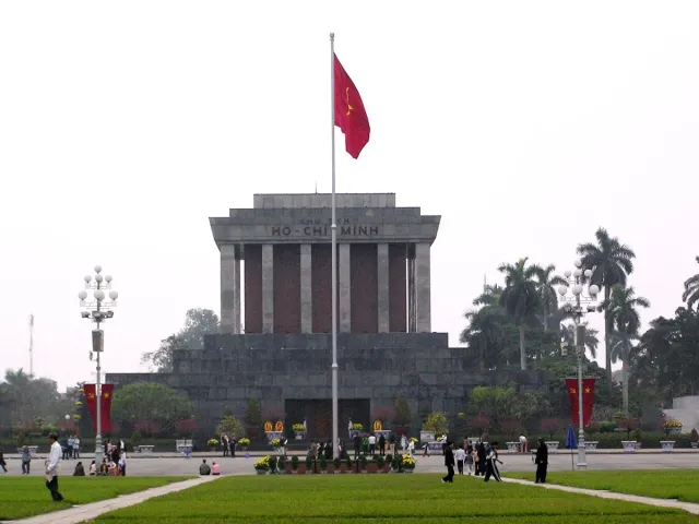A grey stone mausoleum with a red flag flying in the square in front