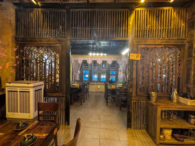 An interior with dark carved wooden partitions, a tiled floor and tables in the inner room