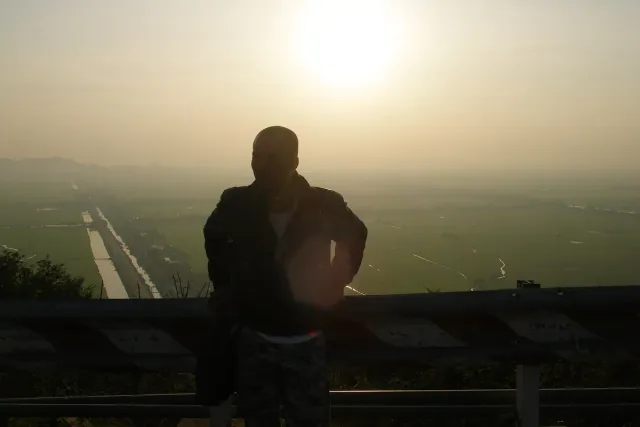 The silhouette of a person against a hazy sunset over a plain