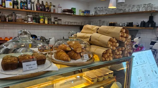 A pastry counter with glass cloches over croissants, paper wrapped baguettes and shelves of bottles