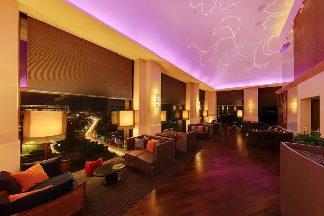 A lounge with sofas and a wooden floor beside tall windows overlooking the city at night