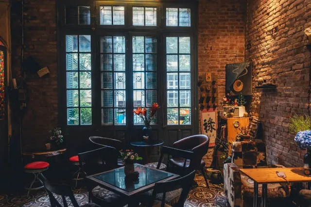 A dim space with brick walls, tall French doors, leather armchairs and a patterned tile floor