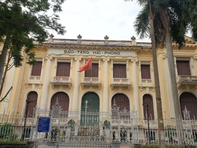 A yellow colonial building with columns and arched windows, a white iron fence in front