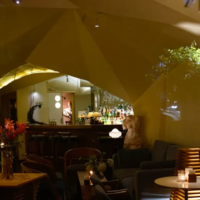 A warmly lit space with a faceted sculpted ceiling, a counter with stools and armchairs