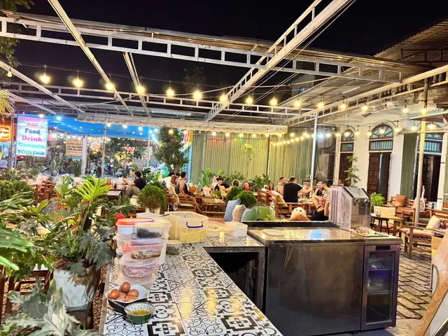 A courtyard lit in the evening with strings of bulbs, green plants and diners at the tables