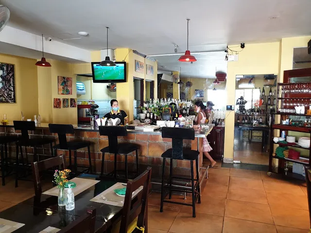 A bar with black stools, yellow walls and red pendant lamps hanging above it