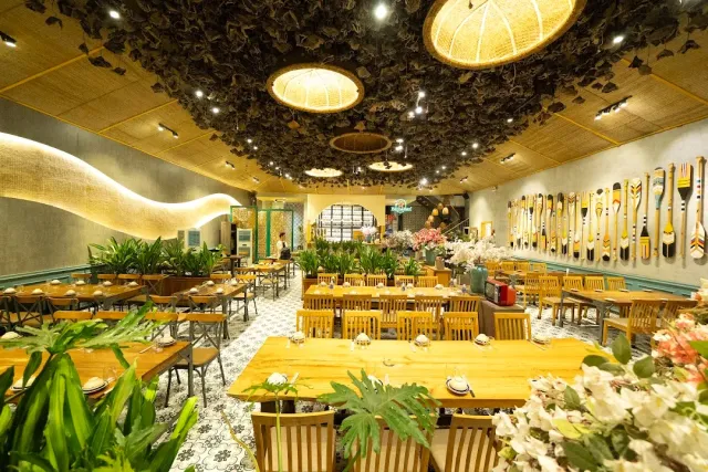 A large space with a dried leaf ceiling, giant straw lamps and a wall of decorated paddles