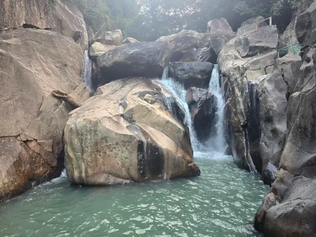 A waterfall running between huge granite boulders into a greenish pool