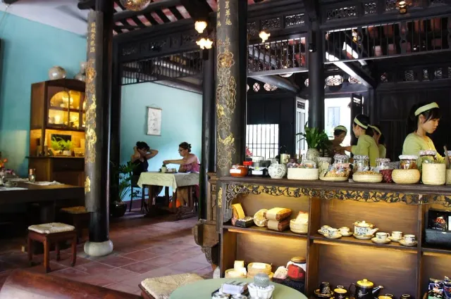 A traditional wooden building with dark columns, a ceramics display case and staff in green