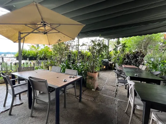 An outdoor terrace under a green awning with a parasol, grey metal chairs and green pots