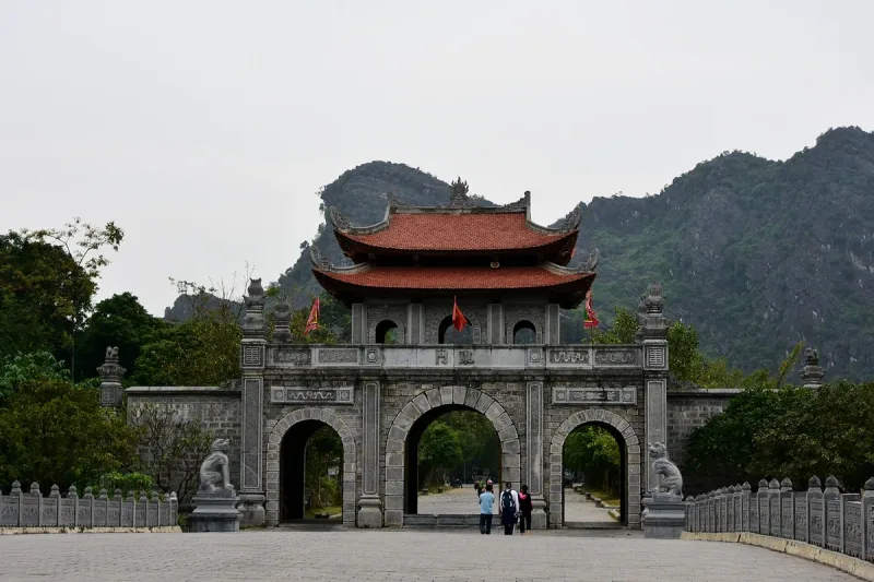 The three-arched stone gate of the Dinh Tien Hoang temple, with a red tiled roof and the Hoa Lu karst cliffs behind
