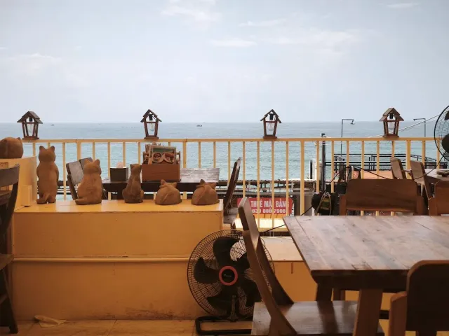 A terrace with a yellow railing, animal figurines on the ledge, wooden tables and a sea view