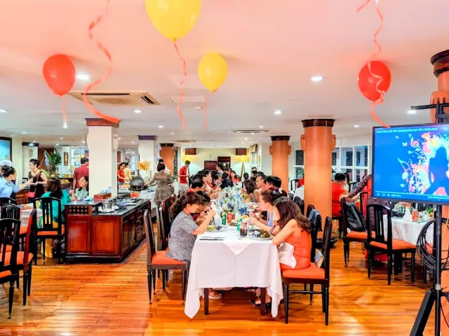 A large hall with a wooden floor, orange columns, balloons at the ceiling and families at tables