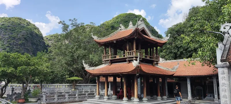 The two-storey wooden pavilion in the courtyard of Thai Vi Temple, with the green karst hills of Tam Coc behind