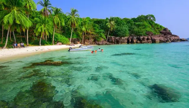 Clear turquoise water over rocks, a white beach with palms and a moored speedboat