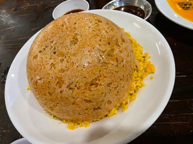 A crisp dome of fried rice on a white plate, beside small bowls of dark sauce