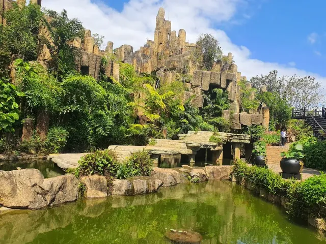 A terraced rock garden with stacked stone columns, greenery and a green pond at its foot