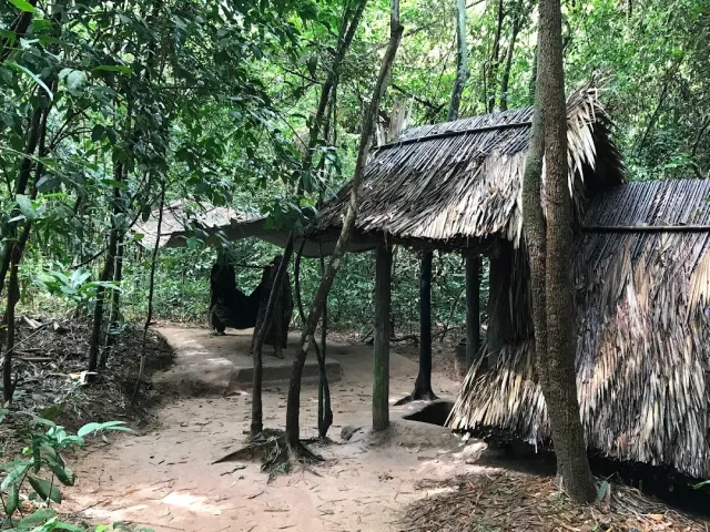 Thatched roof shelters among trees along a dirt path in the forest