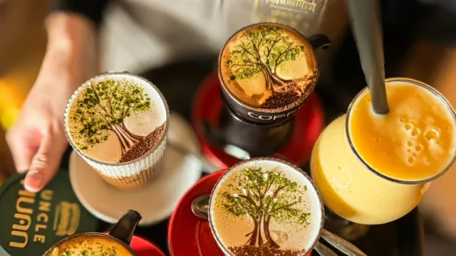 An overhead view of three cups with a tree drawn in the foam and a glass of yellow drink beside them