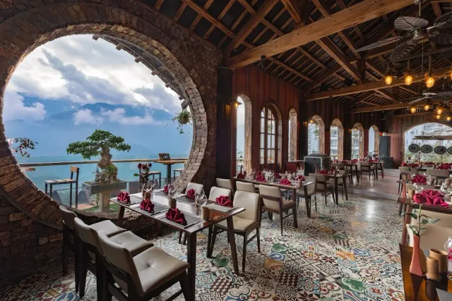 A dining hall with a round brick window onto the mountains, a patterned tile floor and set tables