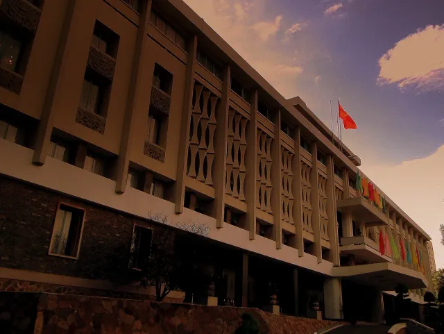 The wide facade of a modernist palace with concrete screens and a flag on the roof