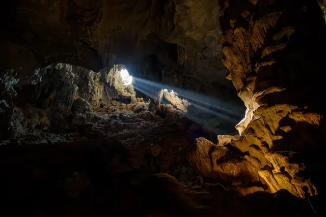 A large cave chamber with a shaft of light falling on stalactite columns