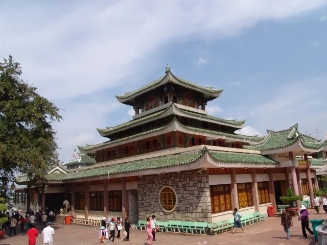 A multi tiered hall with green tiled roofs and visitors crossing the plaza