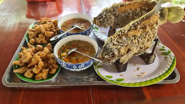 A fried fish standing upright on a holder, beside bowls of soup and plates of fried dumplings