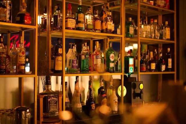 Lit brass shelves loaded with liquor bottles in warm light