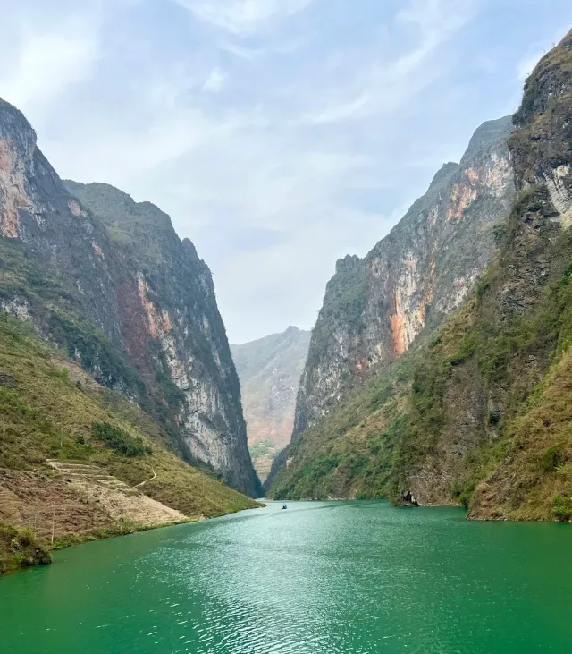 Turquoise colored water flowing between tall steep cliffs, a small boat in the distance