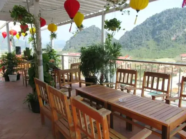 A terrace with hanging silk lanterns, wooden tables and a view of the limestone mountains opposite