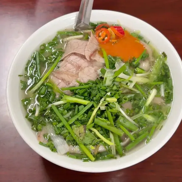 A bowl of beef soup loaded with chopped green onion, meat slices and a spoonful of chili sauce