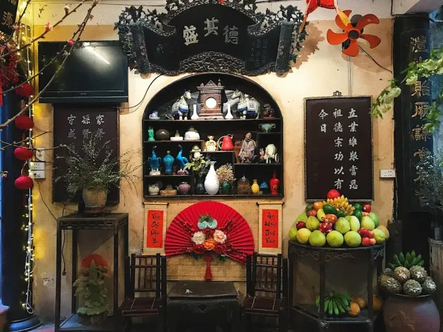 A traditional corner with a carved wooden shelf, porcelain, a red paper fan and a pile of fruit