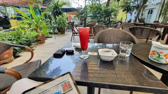 A marble table in the garden with a red drink in a tall glass, a small cup and a glass of water
