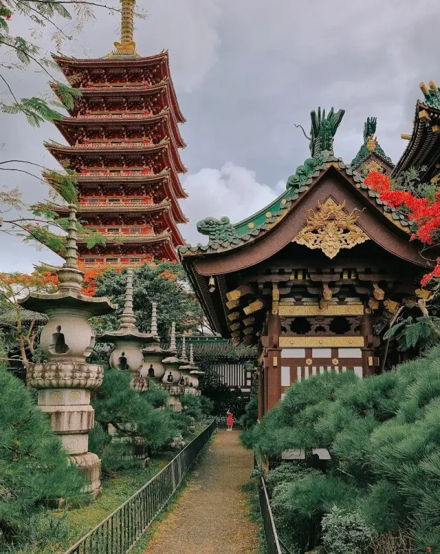 A tall red multi story tower beside a green roofed hall, a path between stone lanterns
