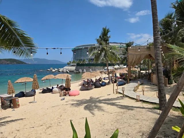 A sandy beach with straw parasols and colorful beanbags facing turquoise water