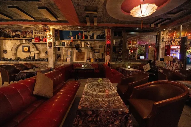 A dim lounge with red leather sofas, crowded shelves and a paper lamp from the ceiling